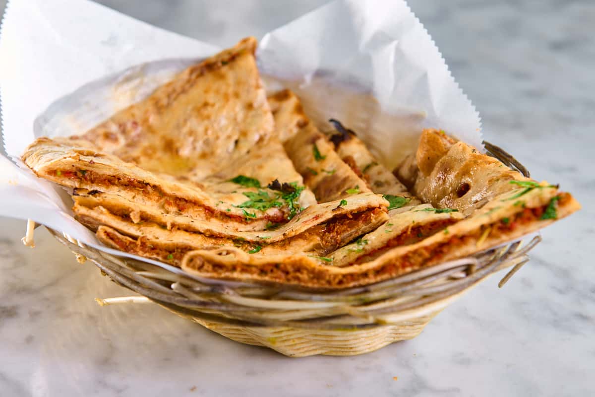 Basket of sliced stuffed naan bread topped with fresh cilantro, featuring crispy paneer naan and spiced garlic naan — traditional Indian flatbread served warm.