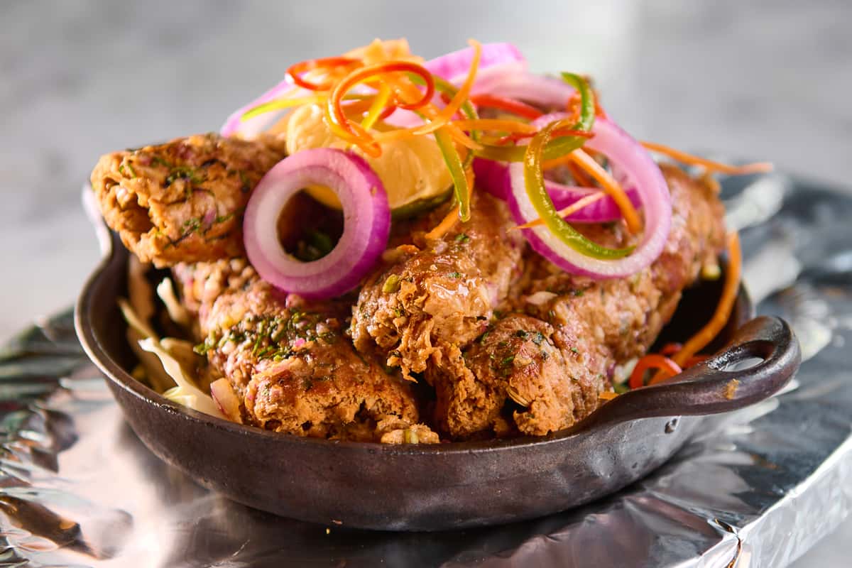 Crispy fried chicken pakora served in a sizzling skillet with shredded cabbage, red onion rings, fresh lime, and julienned peppers — flavorful Indian appetizer with herb seasoning.
