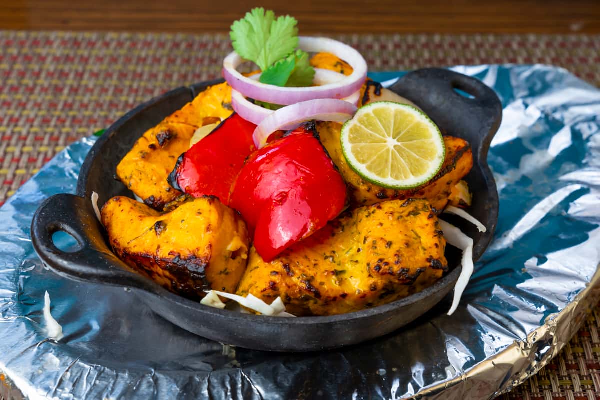 Grilled paneer tikka served in a sizzling platter with charred bell peppers, onion rings, and a fresh lime slice—flavorful Indian tandoori appetizer garnished with herbs.
