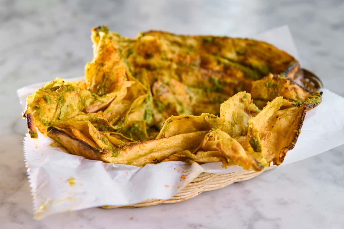 Basket of crispy onion and spinach pakoras drizzled with green herb chutney — golden Indian fritters served hot with spiced gram flour batter.