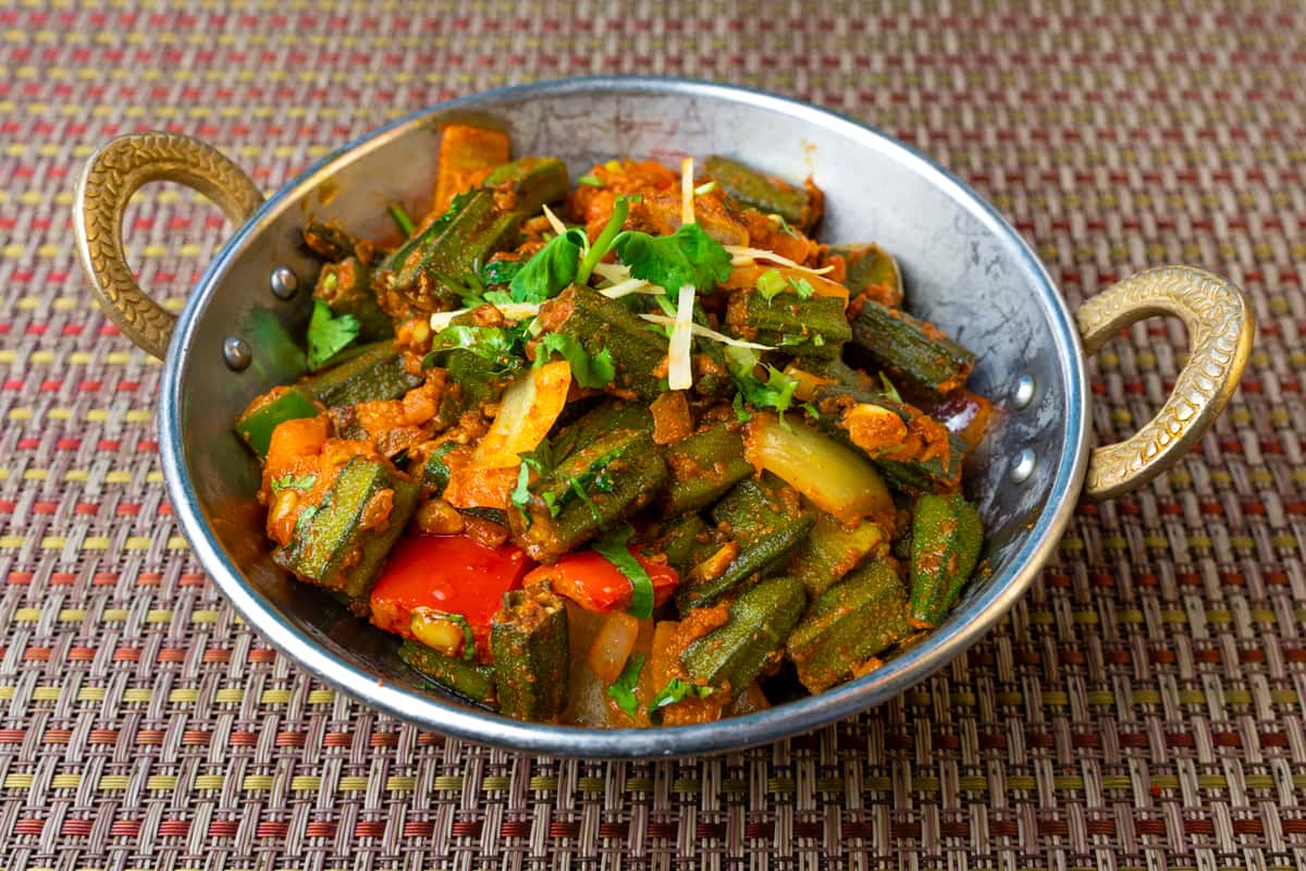 Bhindi masala (okra curry) sautéed with onions, tomatoes, and spices, served in a traditional Indian karahi bowl and garnished with fresh cilantro and ginger.