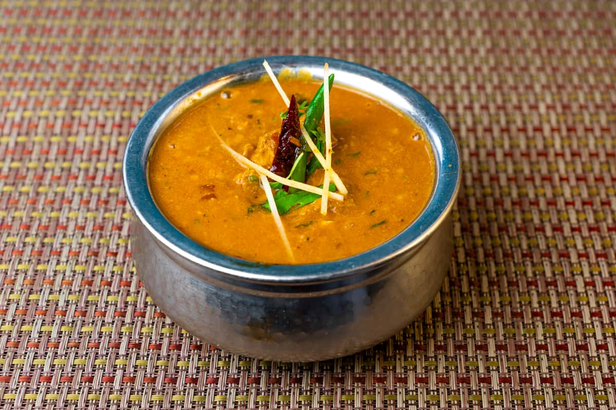Indian lentil dal curry in a metal bowl, garnished with ginger juliennes, green chili, and dried red chili—warm spiced dal with a smooth golden gravy.