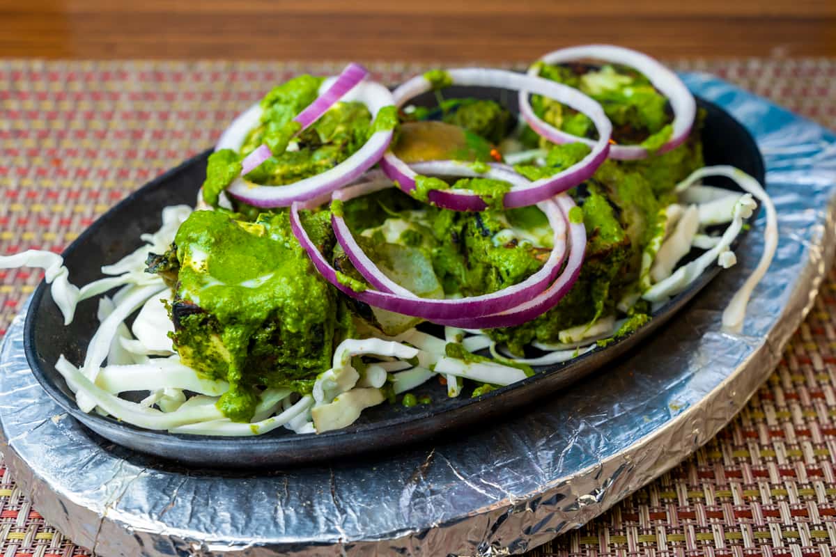 Hariyali paneer tikka — grilled paneer cubes coated in vibrant green herb marinade, served on a sizzling platter with onions.