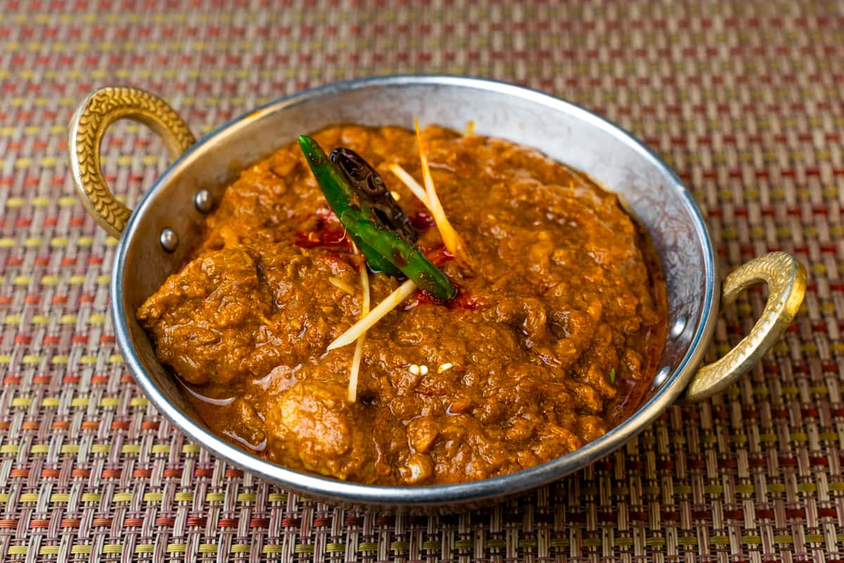 Rich Indian egg curry in a thick spiced tomato-onion gravy, garnished with whole green chili and julienned ginger, served in a traditional metal karahi bowl.