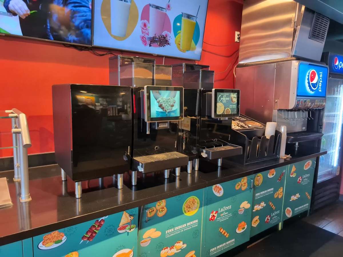 Self-serve beverage station in a modern Indian fast-casual restaurant featuring drink dispensers, soda fountain, and colorful menu displays against vibrant red walls.