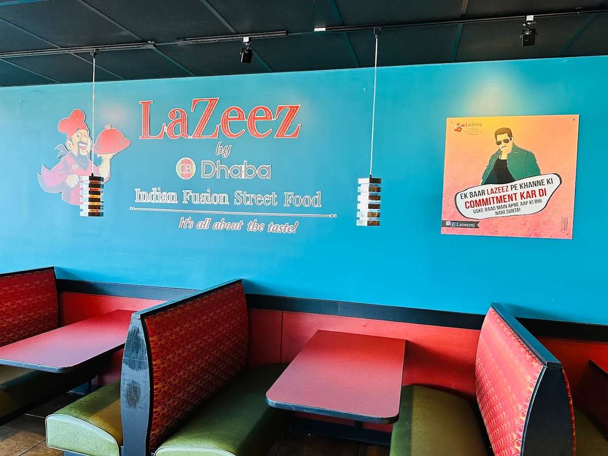 Modern Indian fusion restaurant interior featuring teal walls with "LaZeez by Dhaba" branding, red booth seating, and vibrant decor highlighting a casual, colorful dining atmosphere.