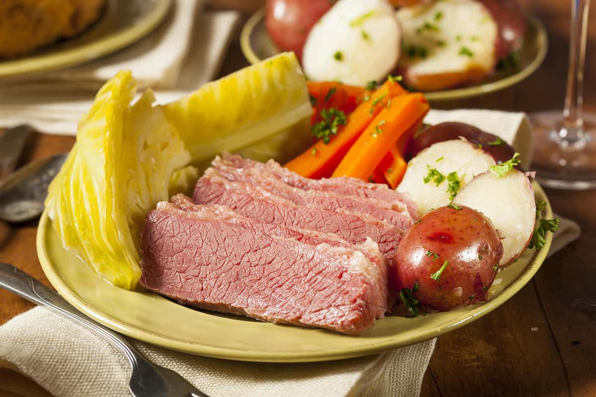 Dish of meat, and carrots, potatoes and cabbage surrounded by other plates with the same food