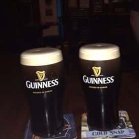 2 full glasses of Guinness with foam at the tops in Guinness branded mugs