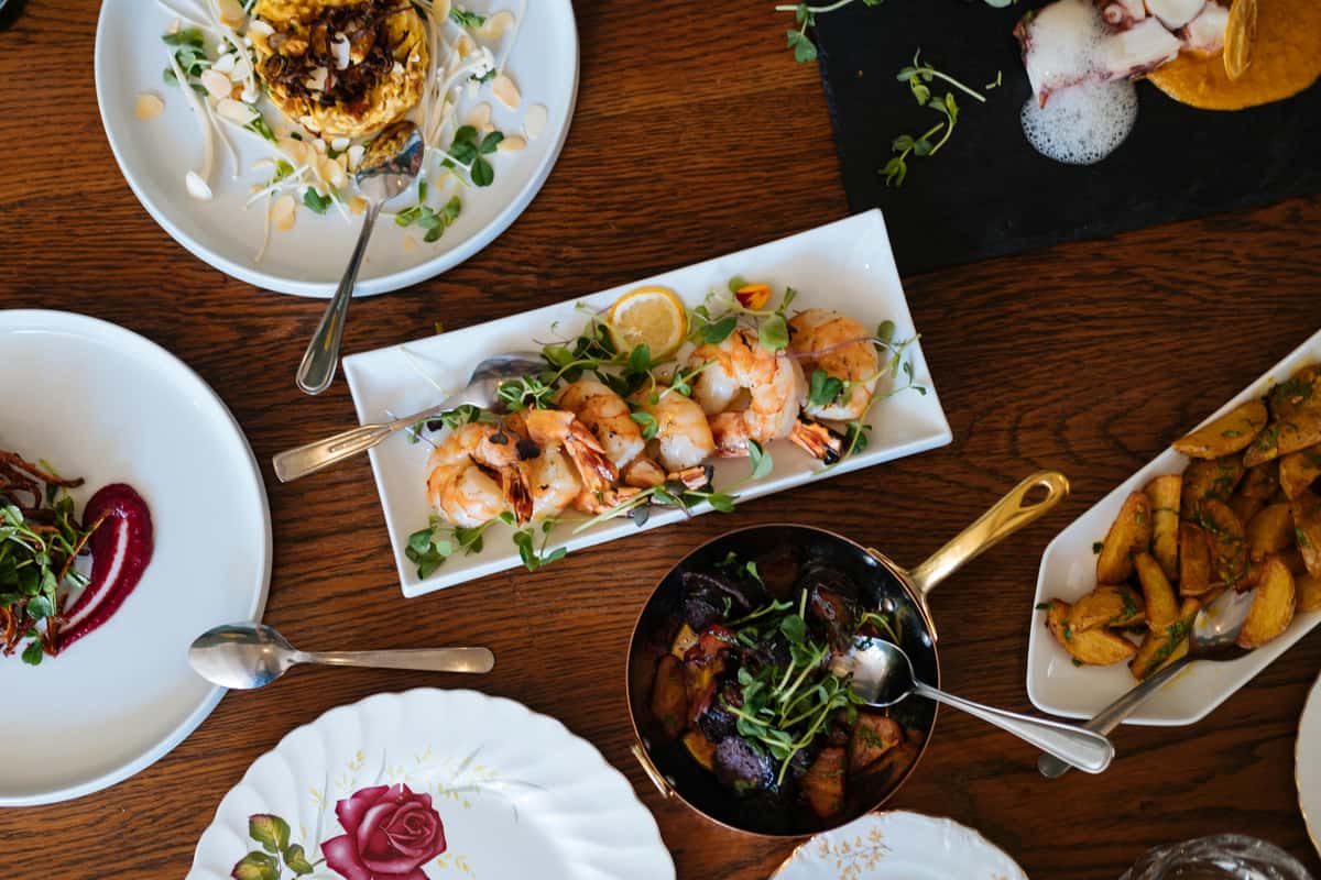 Elegant seafood and vegetable spread featuring grilled shrimp, roasted potatoes, purple root vegetables, and artfully plated garnishes.