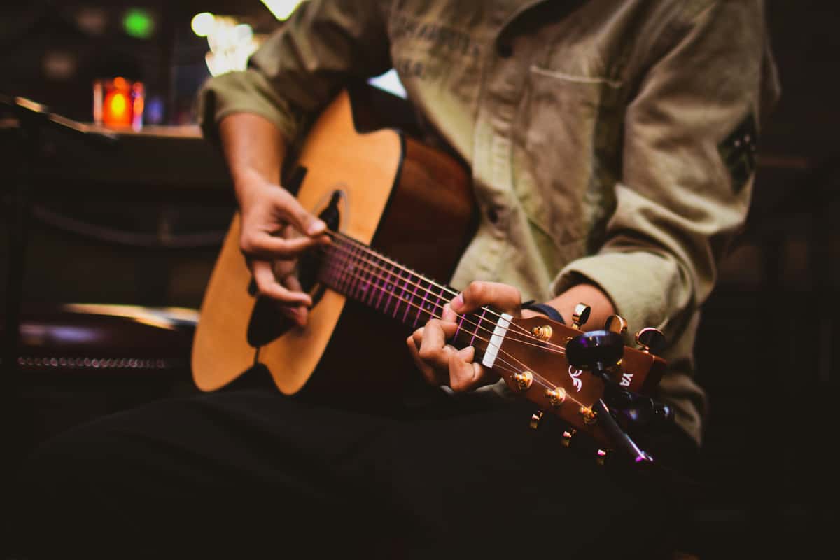 A focused shot of a musician in a tan shirt skillfully playing an acoustic guitar in a dimly lit, cozy setting