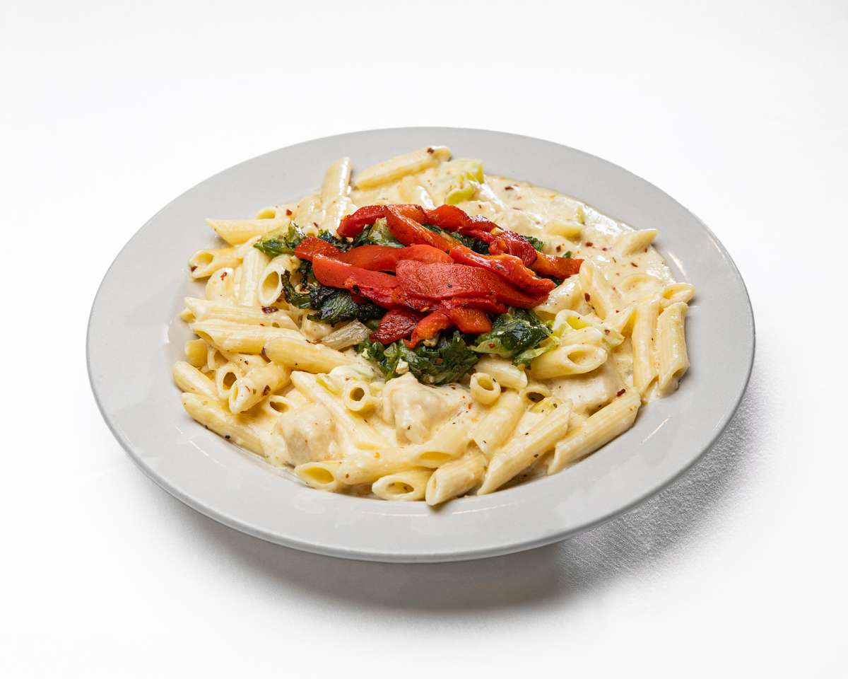 A plate of creamy penne pasta tossed with chicken, topped with sautéed green spinach and bright red roasted peppers.