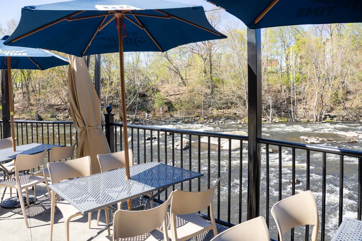 outdoor restaurant patio with blue umbrellas, riverside views, and casual dining tables