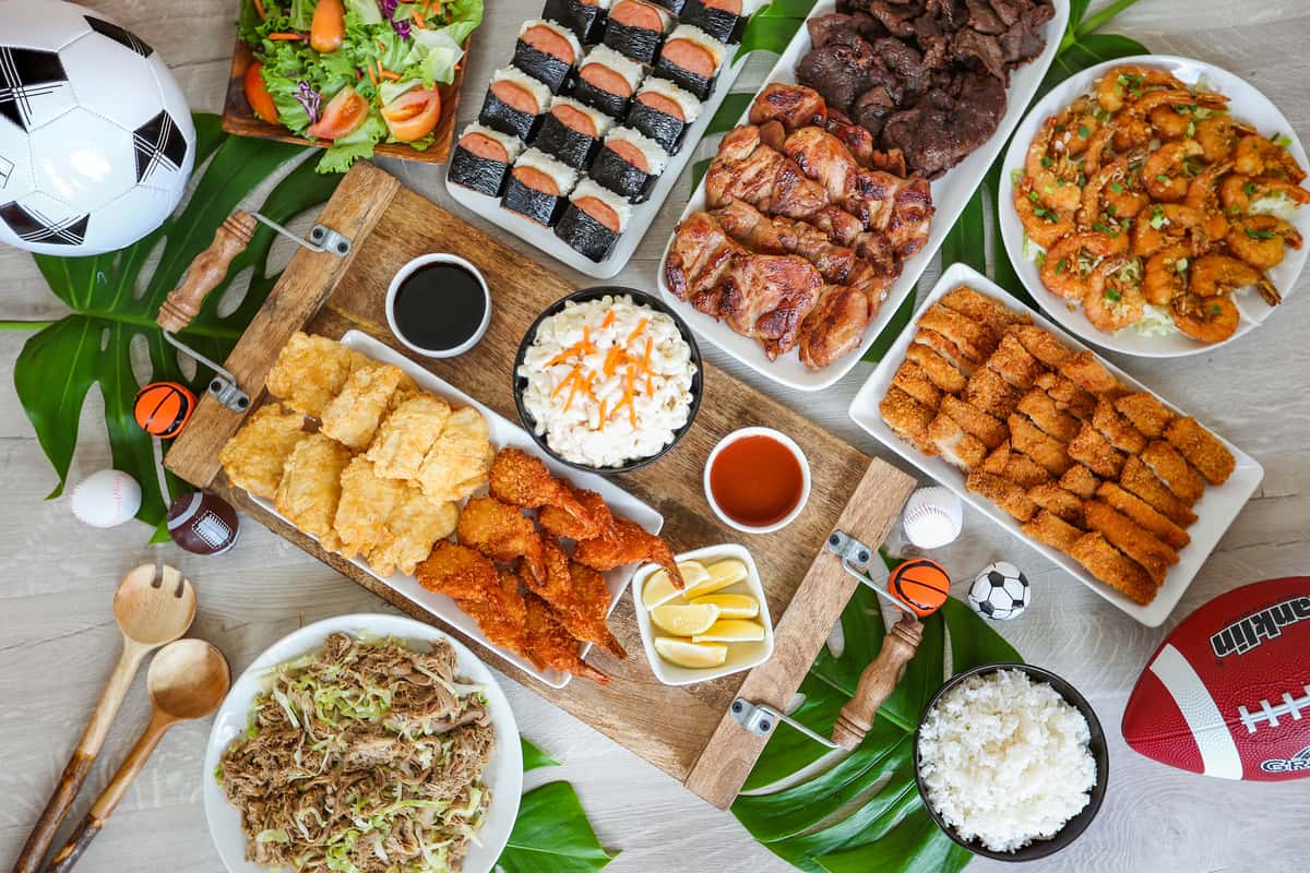 Catering party trays filled with BBQ chicken, masubi, pulled pork and sides