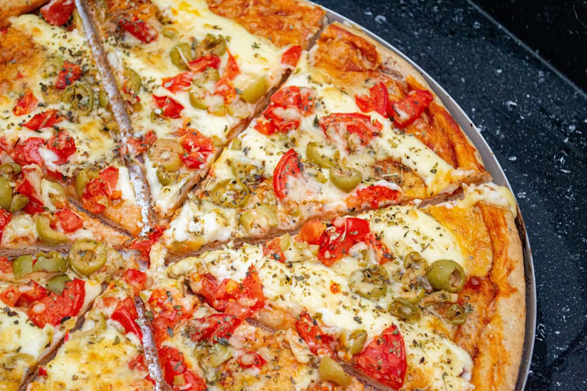 Vegetarian pizza topped with tomatoes, green olives, and cheese on a black background.