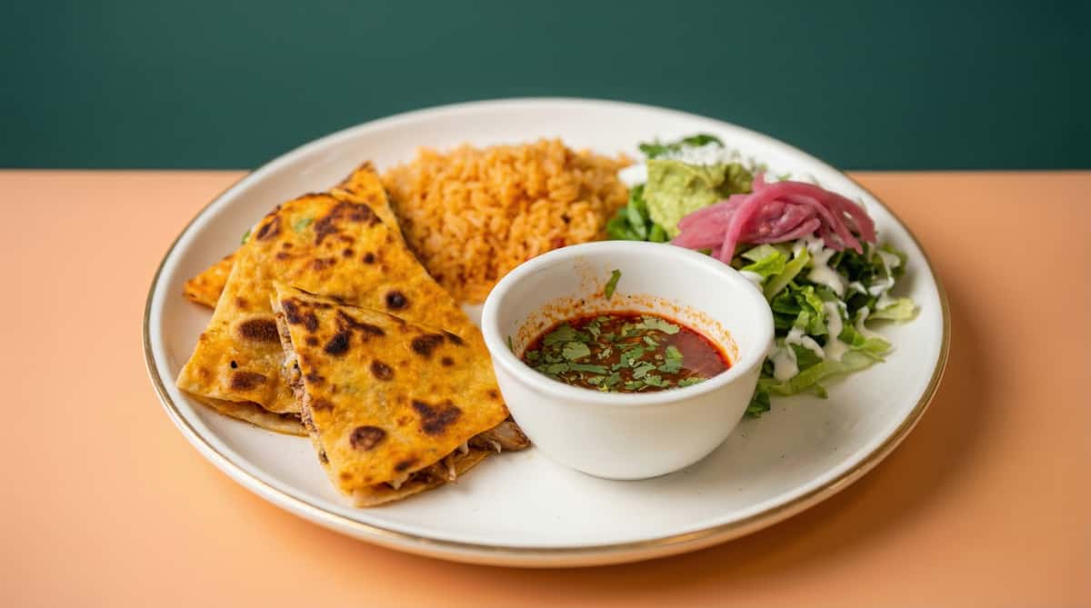 Golden grilled chicken quesadilla served with Mexican rice, fresh salad, guacamole, and red salsa in a casual restaurant setting