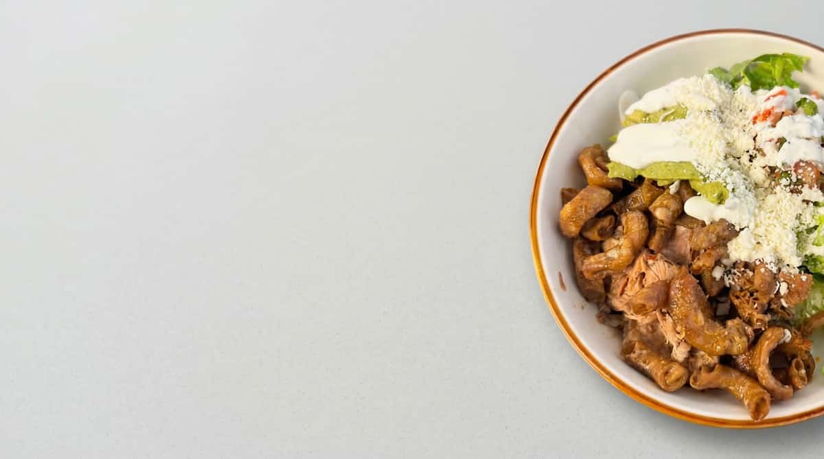 Mexican bowl with grilled meat, guacamole, crema, and queso fresco over seasoned ingredients in a fresh, modern presentation