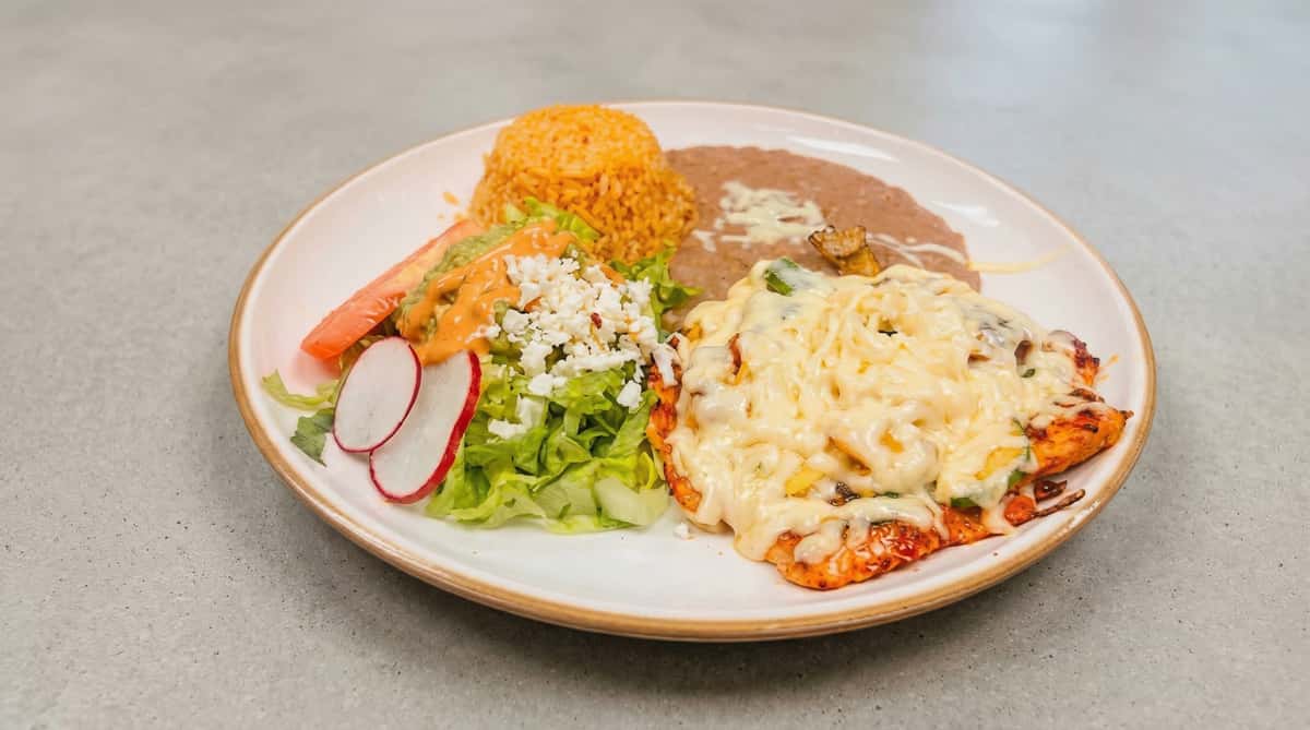 Grilled chicken fajitas topped with melted cheese, served with Mexican rice, refried beans, avocado slices, and fresh toppings
