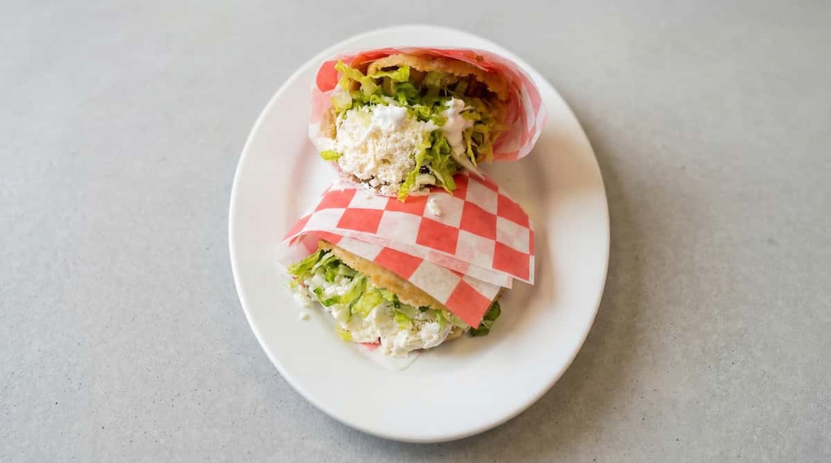 Mexican torta wrapped in paper with fresh lettuce, crema, and queso fresco on a soft roll