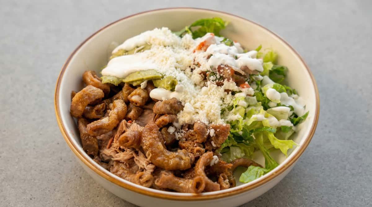 Mexican carnitas bowl with crispy pork, shredded meat, fresh lettuce, guacamole, crema, and crumbled queso fresco