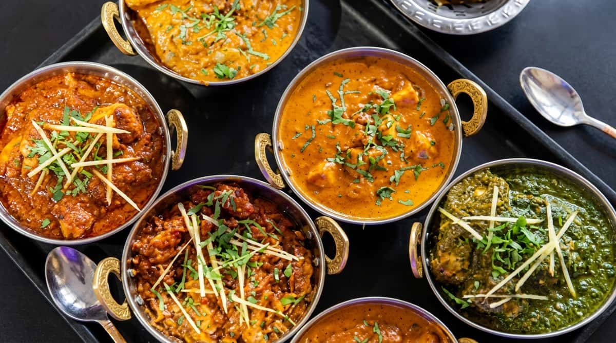 Selection of colourful Indian curries served in traditional bowls with fresh herbs, spices and accompaniments.