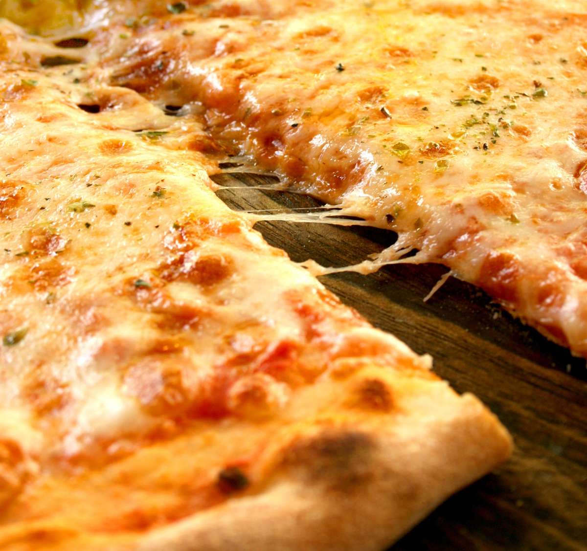 Cheesy pizza slice being pulled away, with melted mozzarella stretching and a crispy golden crust.