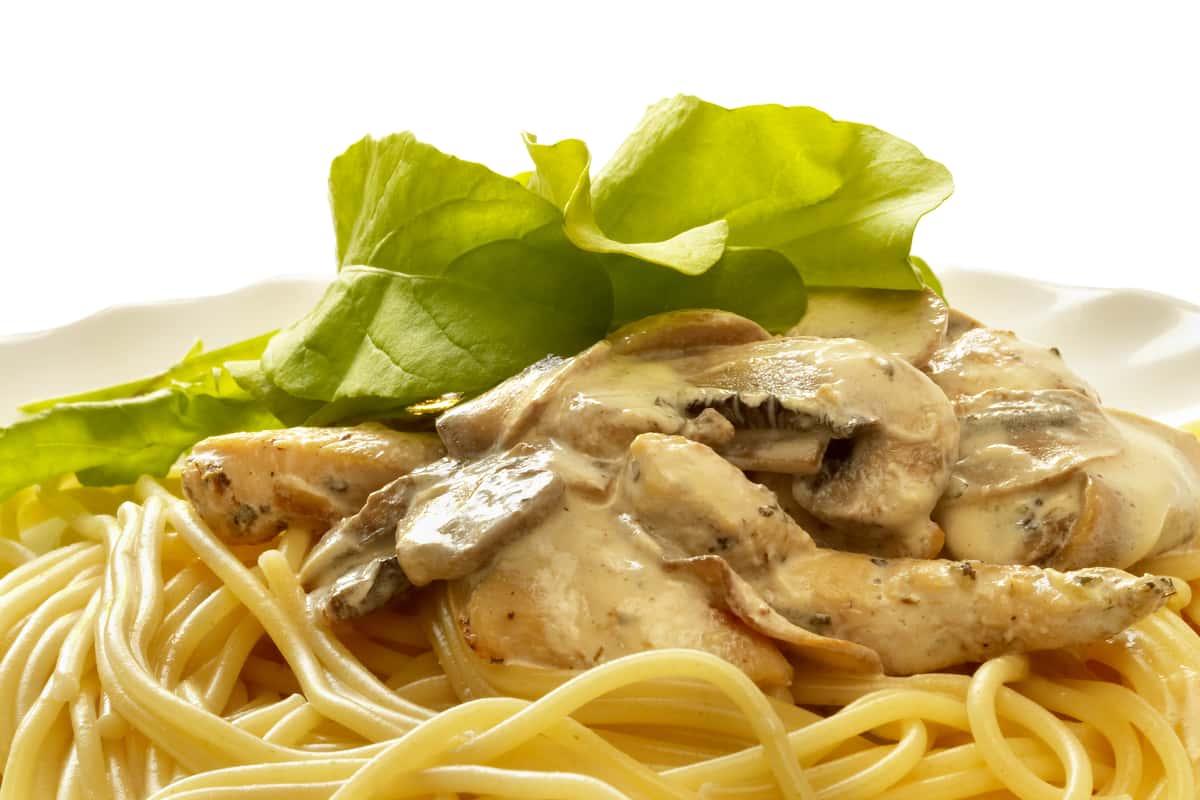 Spaghetti topped with creamy chicken and mushroom sauce, garnished with fresh green lettuce.