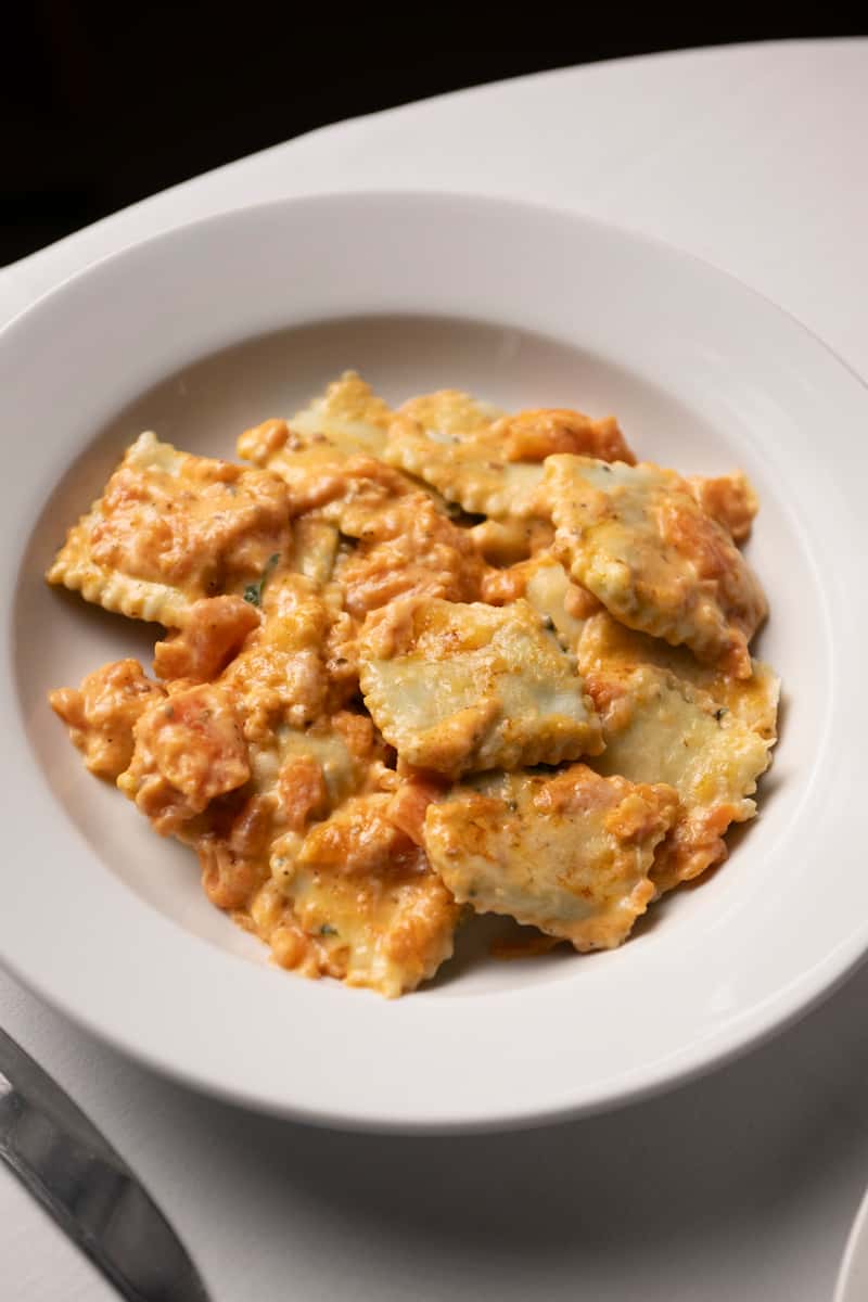 Cheese-stuffed ravioli coated in a creamy tomato sauce, served in a white bowl on a white tablecloth.