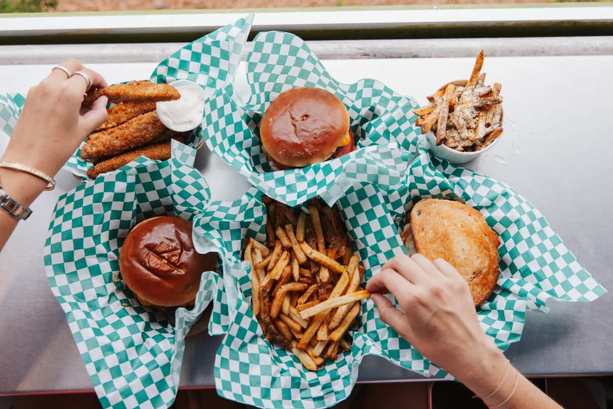 Overhead view of burgers, crispy fries, and casual beachside favorites served on a checkered tray.