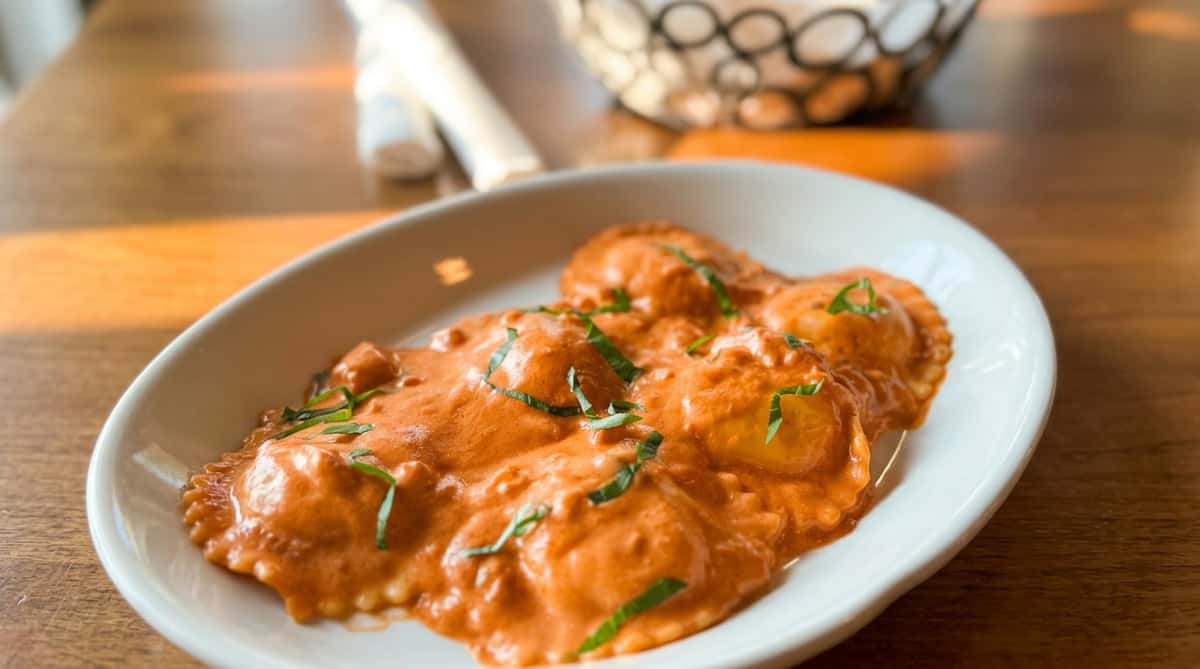 Ravioli in a creamy orange sauce, topped with fresh green basil, served in a white bowl.