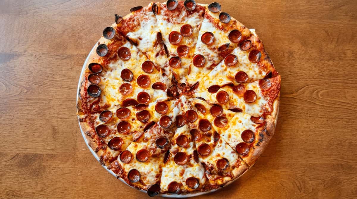 Pepperoni pizza on a metal pan with melted mozzarella and curled, slightly charred pepperoni slices.