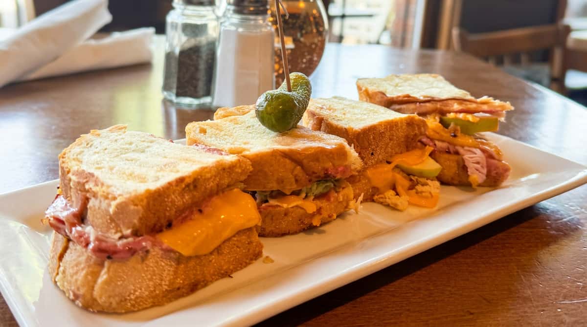 Four different mini sandwiches, one with a pickle on top, on a white rectangular plate.