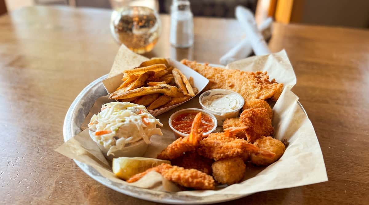 Breaded shrimp with coleslaw, toast, and fries on a white platter