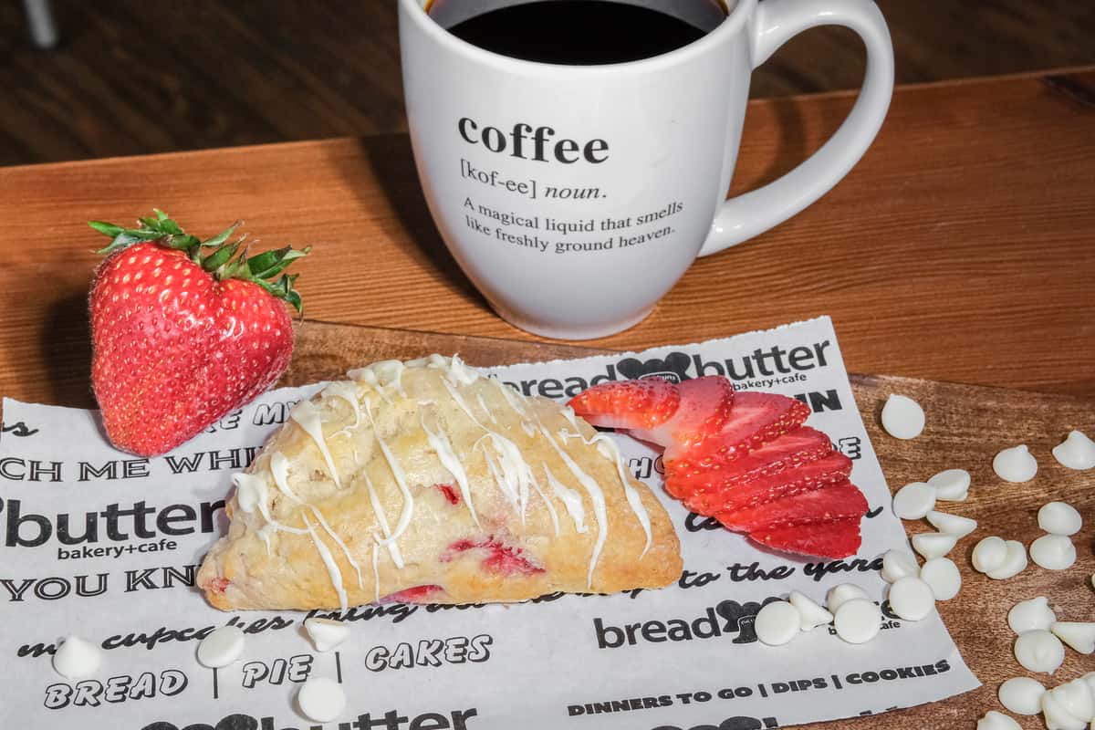 Freshly baked white chocolate strawberry scone drizzled with icing, served with fresh strawberries and hot coffee at Bread and Butter Bakery.