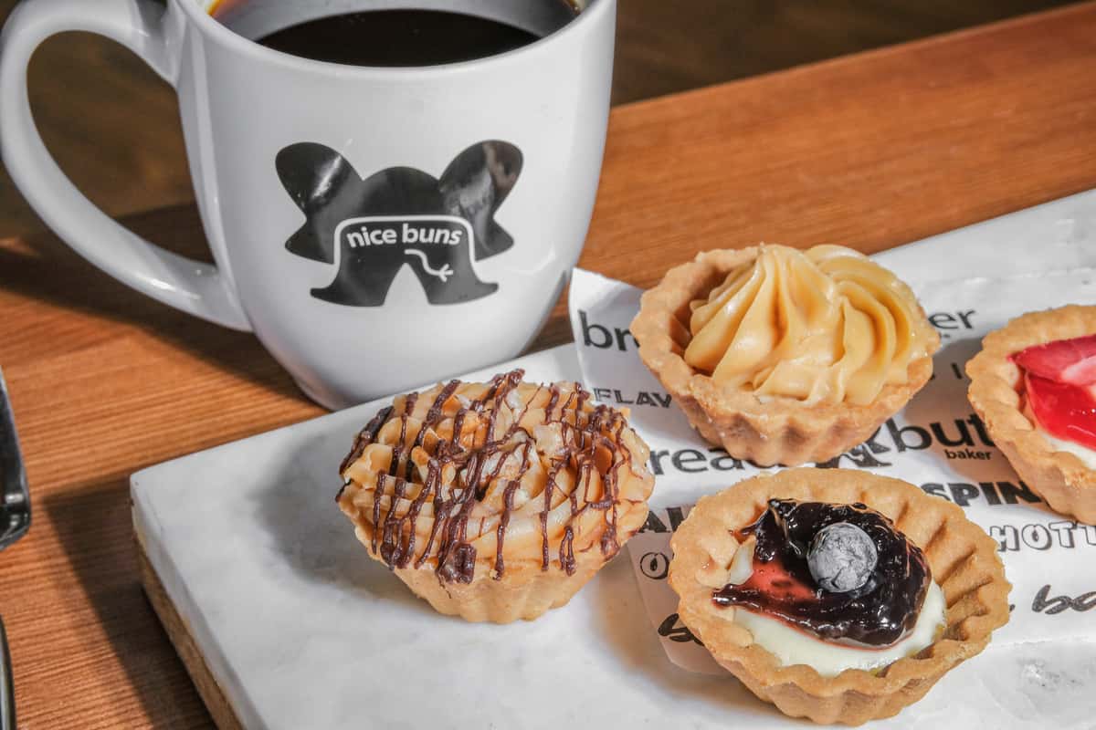 Freshly brewed coffee served with an assortment of handcrafted mini dessert tarts, including caramel, blueberry, strawberry, and coconut chocolate, from Bread & Butter Bakery and Cafe.