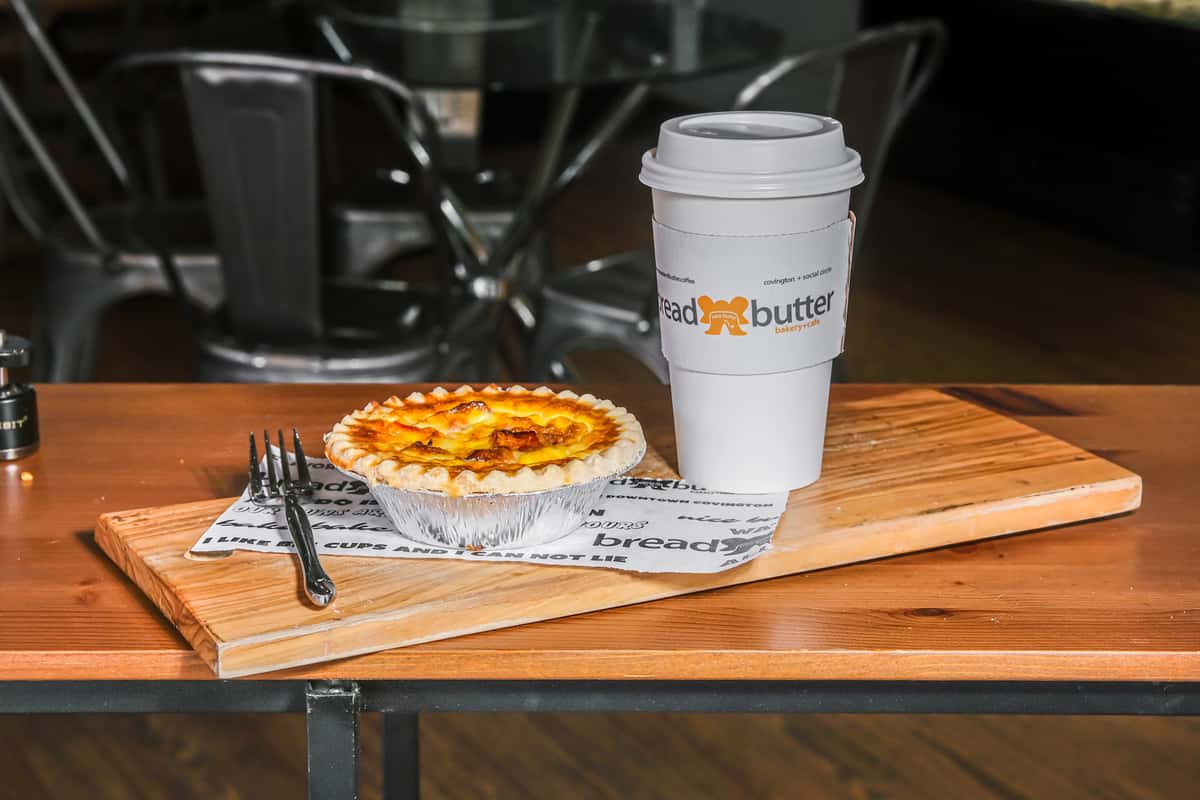 Mini quiche in foil tin with a disposable Bread & Butter coffee cup on a wooden serving board with a fork.