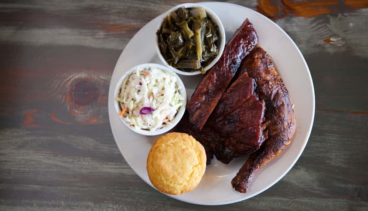 BBQ ribs and chicken on a plate with corn bread, cole slaw and collard greens