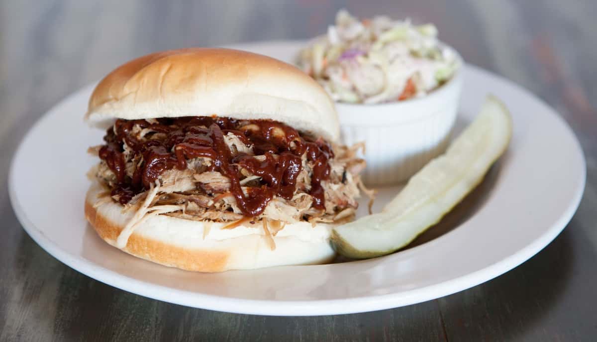 Pulled pork sandwich with BBQ sauce on a bun with a pickle and cole slaw