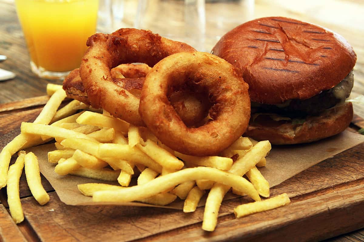 Juicy cheeseburger with a toasted brioche bun, served with crispy French fries and golden onion rings on a wooden board — a classic American pub meal.