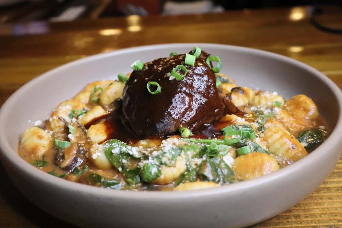 Braised short rib over creamy gnocchi with mushrooms, spinach, and scallions, topped with rich demi-glace in a cozy pub setting.