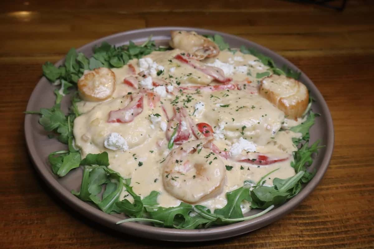 Creamy scallop and crab ravioli topped with goat cheese, roasted red peppers, and herbs over fresh arugula in a cozy pub setting.
