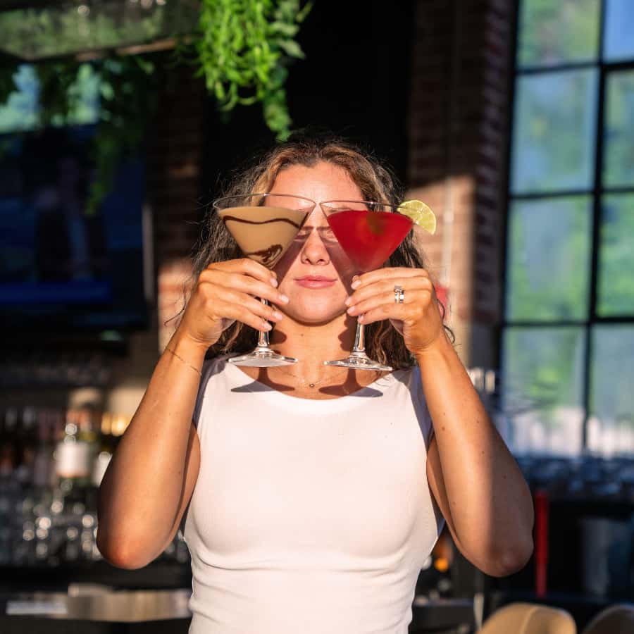 Woman enjoying two colorful cocktails in a lively restaurant setting