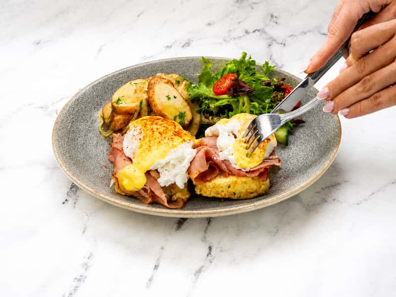 Brunch entrée featuring poached eggs, breakfast potatoes, greens, and hollandaise