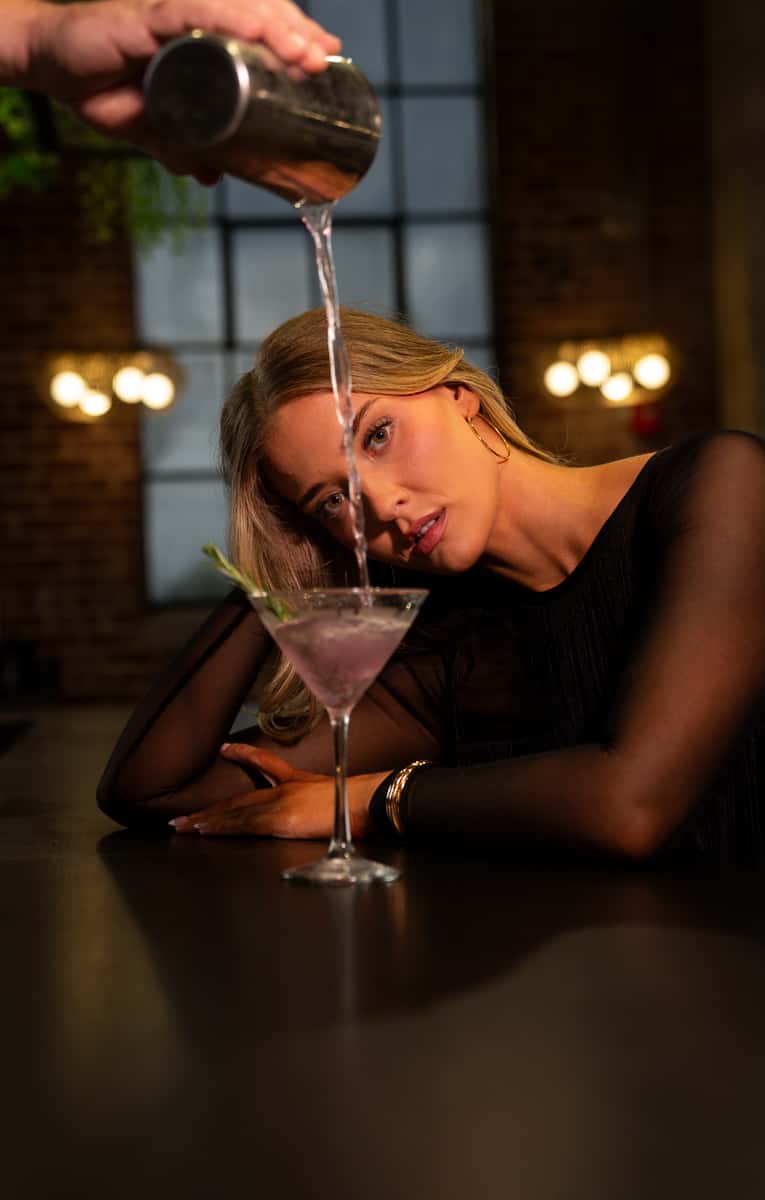 Woman enjoying a signature purple cocktail in an upscale restaurant setting