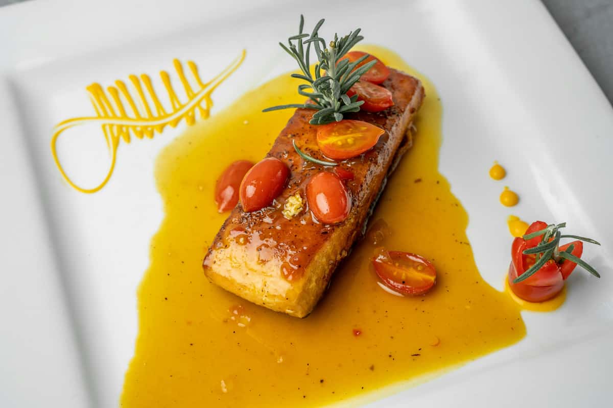 A beautifully plated piece of grilled salmon garnished with cherry tomatoes and fresh rosemary, served with a citrus sauce drizzle.