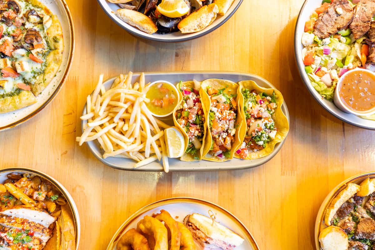 Overhead view of vibrant chicken street tacos topped with fresh pico de gallo and cotija cheese, served with French fries and salsa, surrounded by assorted entrees