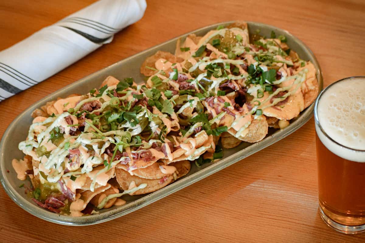 Loaded pub-style nachos topped with shredded meat, jalapeños, fresh cilantro, and drizzled with creamy cheese sauce, paired with a frothy pint of craft beer.