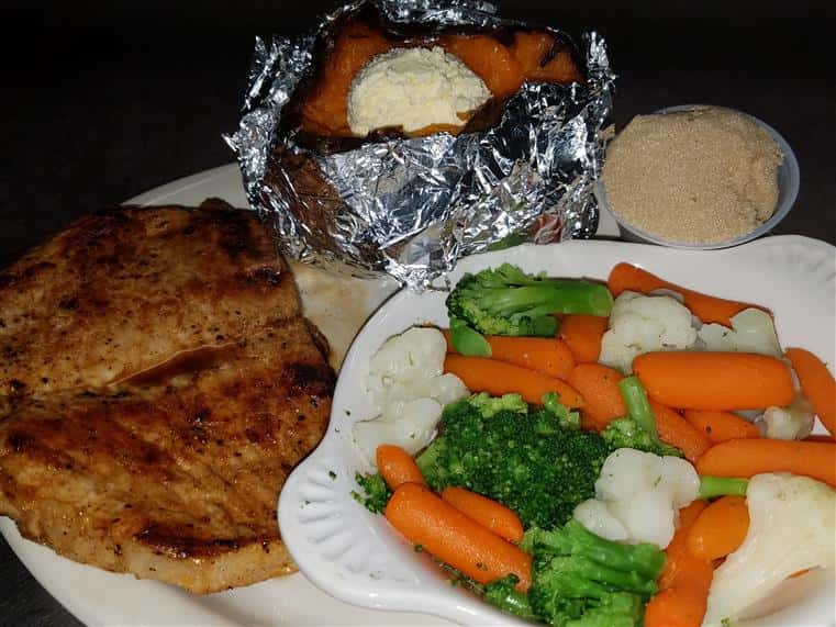 grilled porkchop with a plate of veggies and a baked sweet potato with a side of cinnamon butter