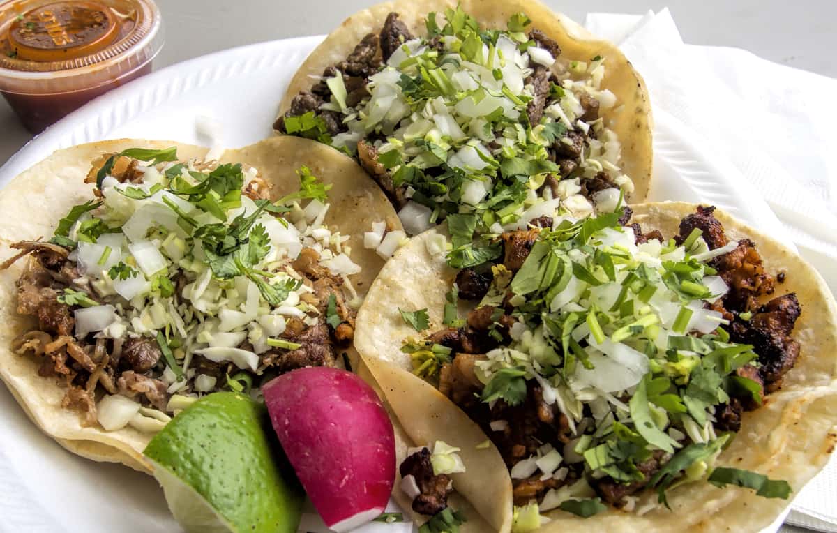 Three Pinches Tacos with meat, diced onion, and cilantro, served with lime, radish, and salsa.