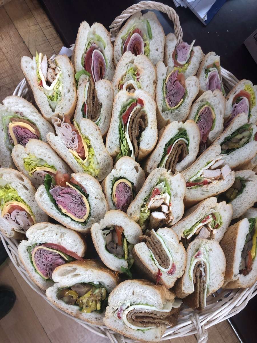 A basket filled with sliced and pre-made Italian and American heroes. 