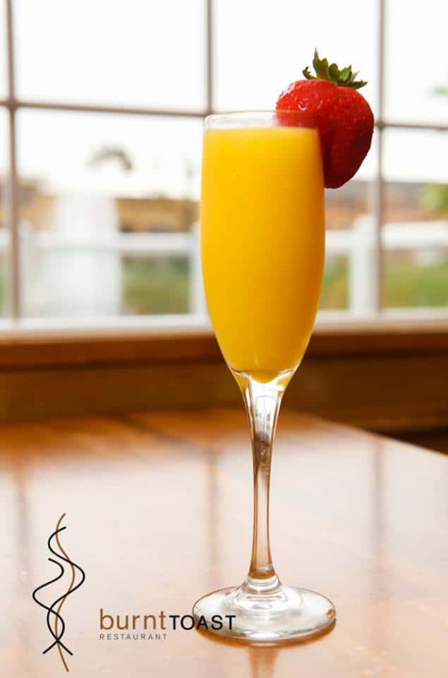 Mimosa in a champagne glass with a strawberry on the rim on a wooden table-top